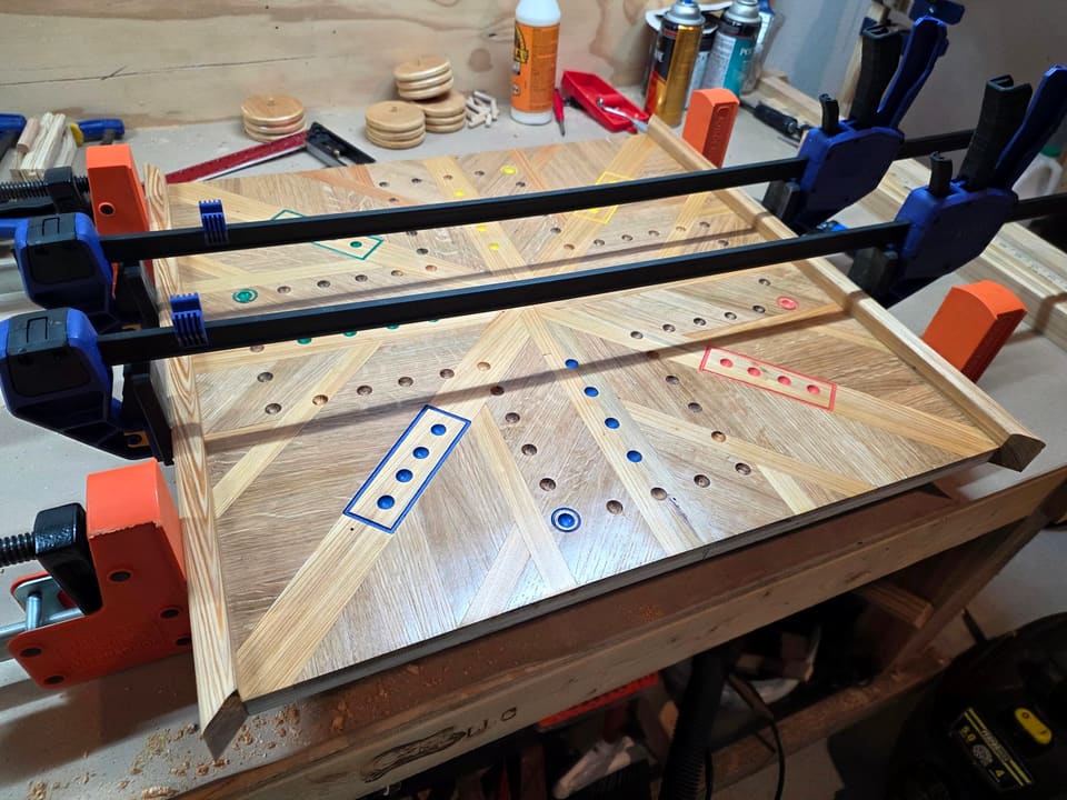 Marble game board in clamps during glue-up, drilled tracks and colour dots visible