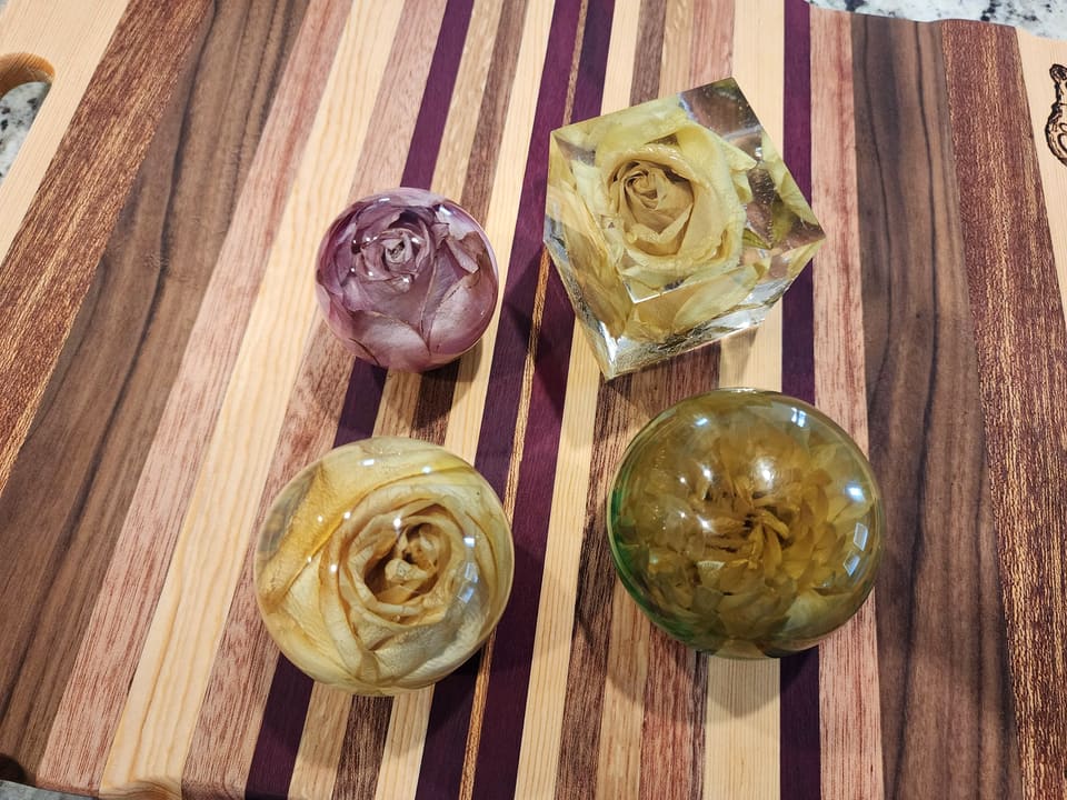 Four preserved rose keepsakes in resin, two spheres and two cubes, on a striped hardwood board