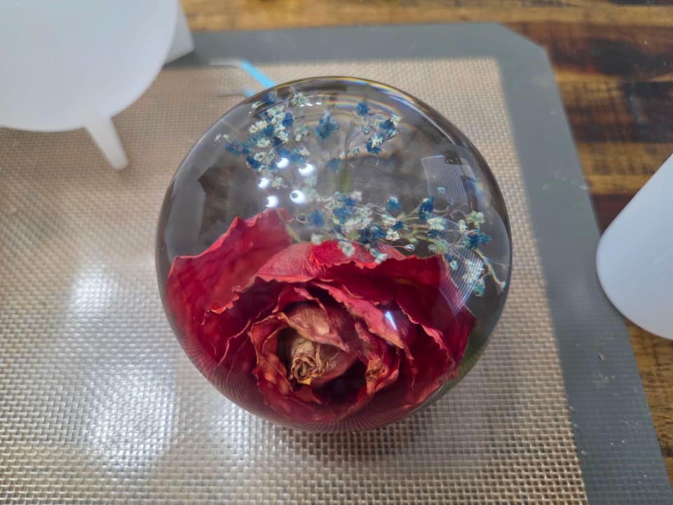 Red rose and small blue flowers preserved in a resin dome