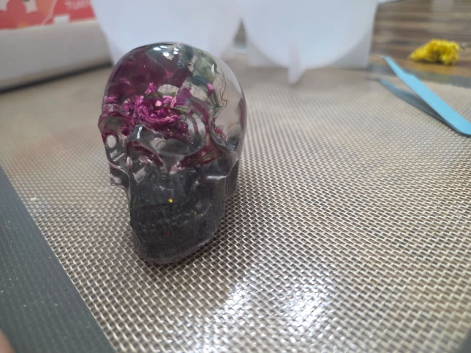 Dark translucent resin skull with magenta dried flowers inside, front view