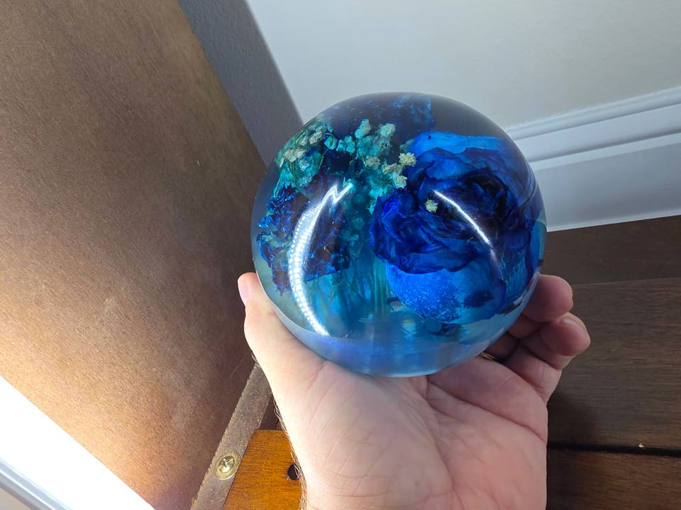 The blue rose resin sphere held in one hand for scale