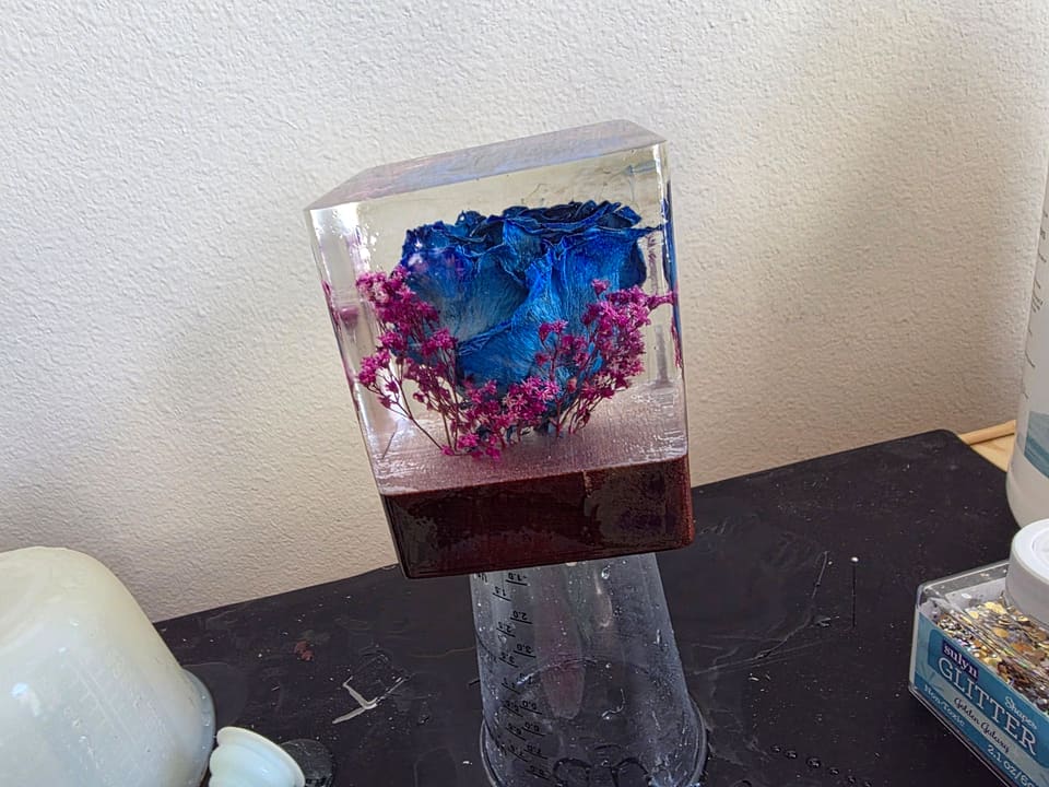 Blue rose resin cube on a dark wood base, set on a shelf against a white wall