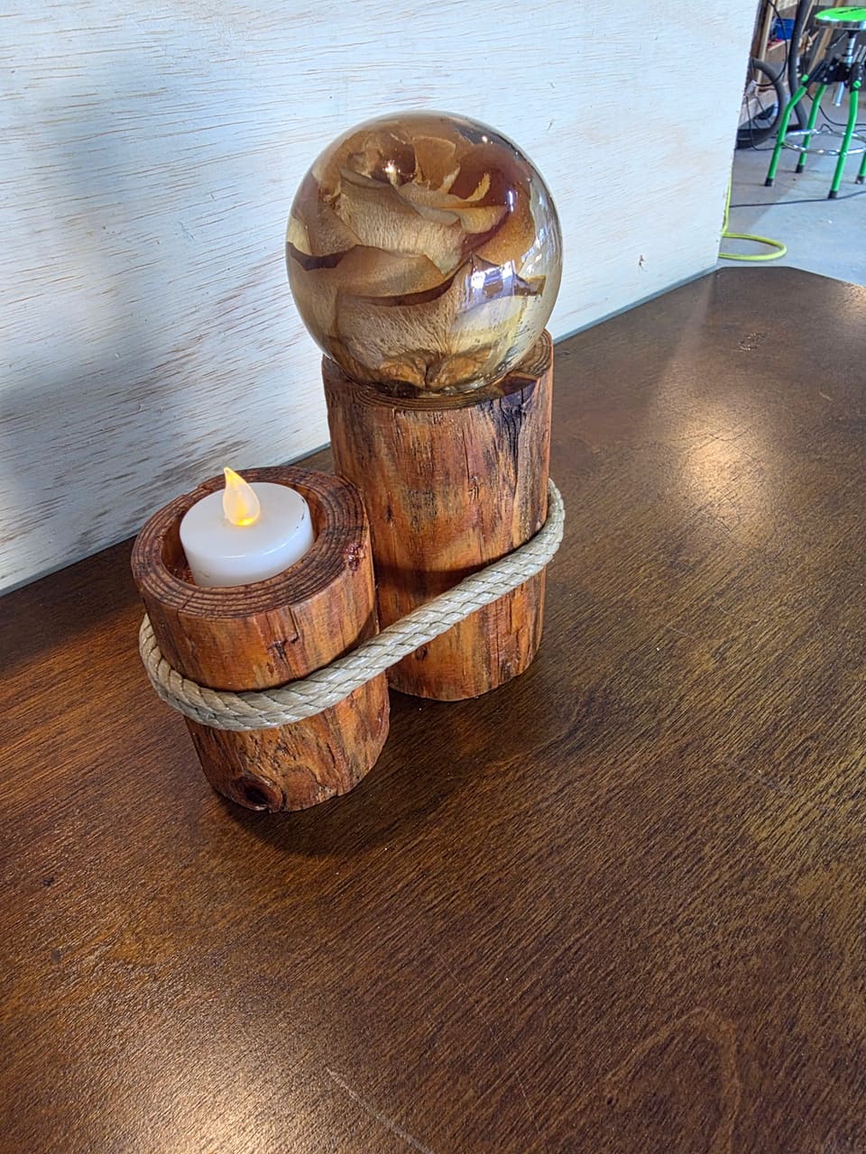 Two short log candle holders bound together with rope, one holding a flameless candle and one topped with a resin sphere