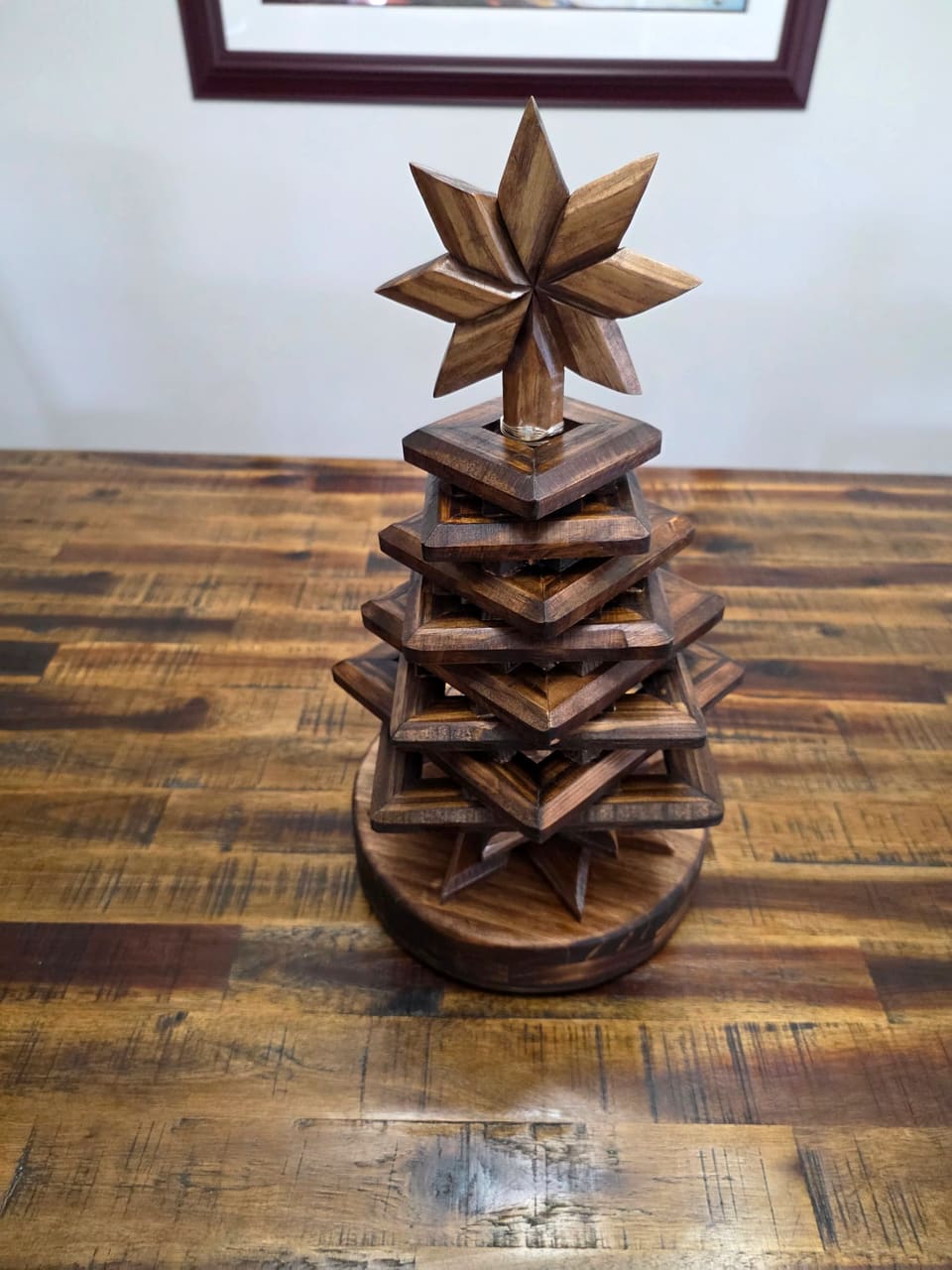 Stacked wood Christmas tree with a carved star on top, front view on a rustic wood table