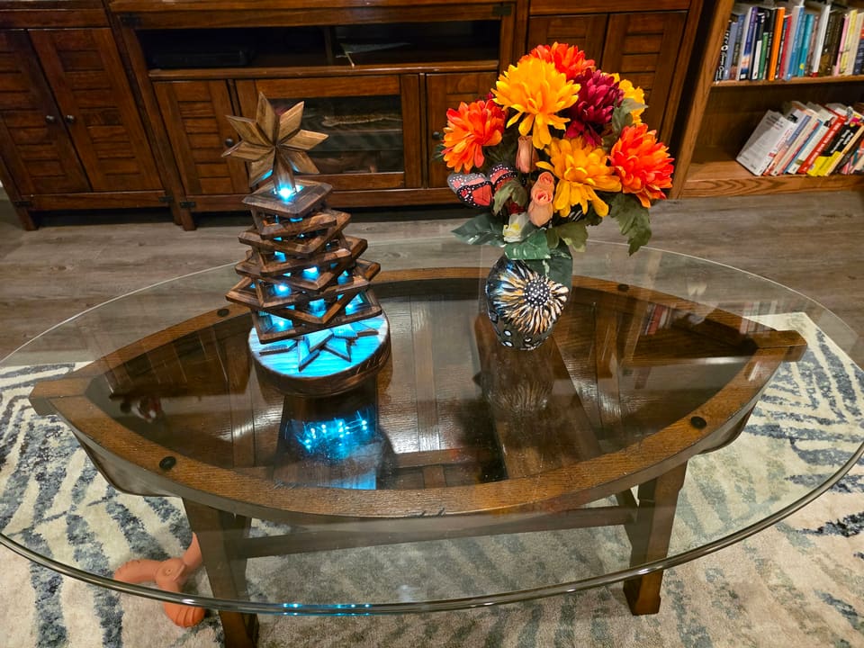 The stacked wood tree lit with teal light on a glass coffee table beside a vase of flowers