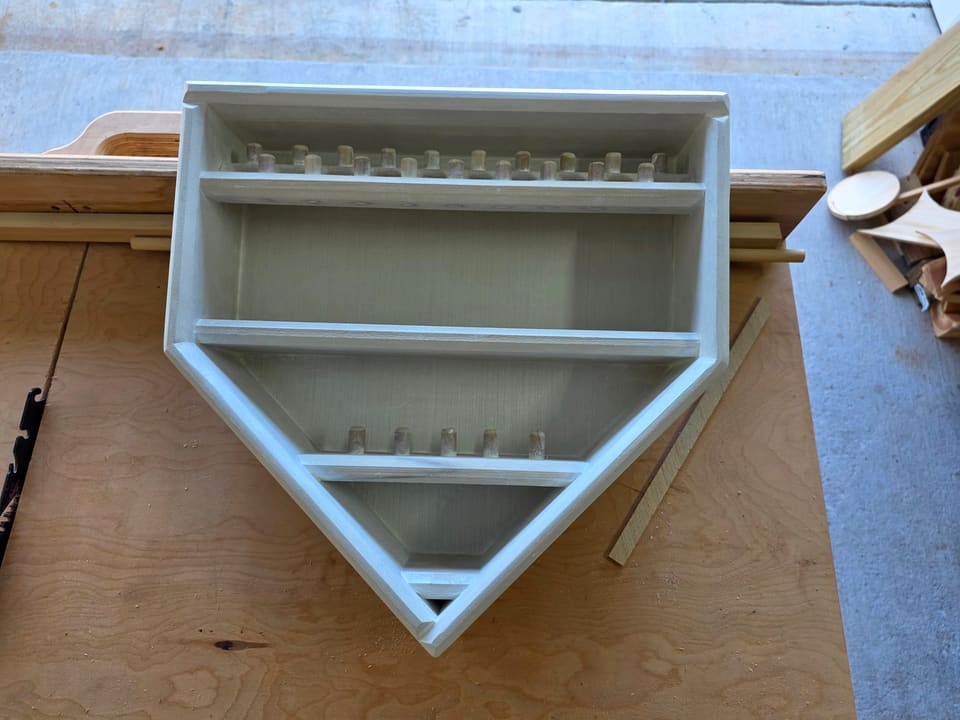 White home-plate-shaped wall display case with shelves and slots, in progress on the workbench