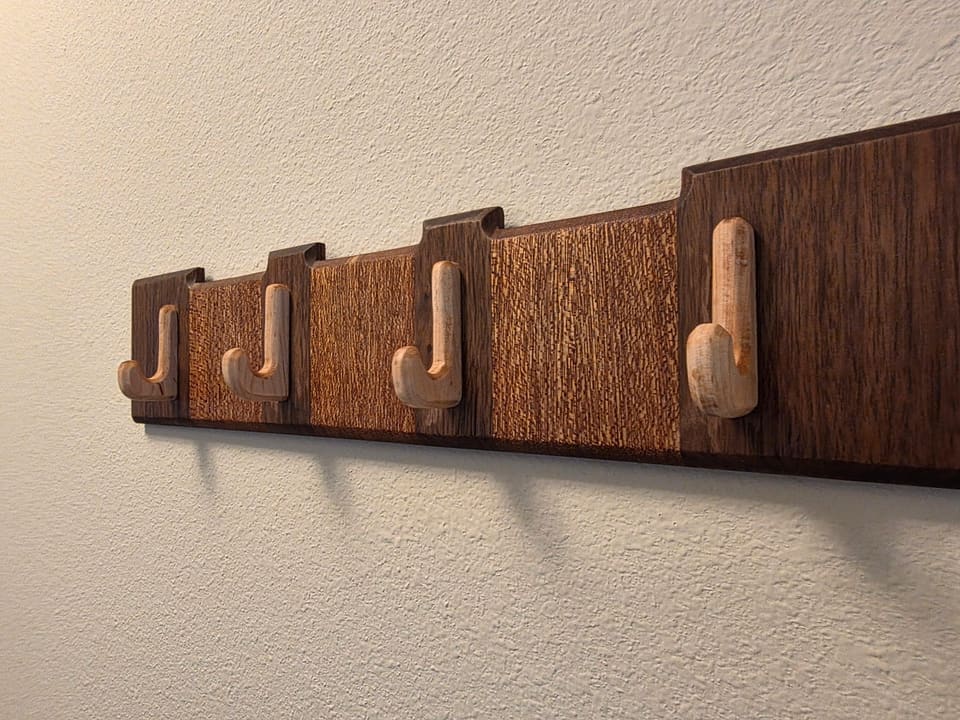 Wall-mounted rack with light wood hooks on a two-tone dark wood board