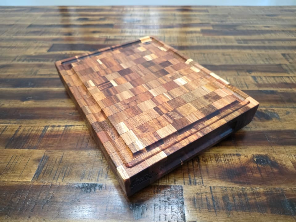 End-grain cutting board of mixed hardwoods with a groove around the edge, on a plank table