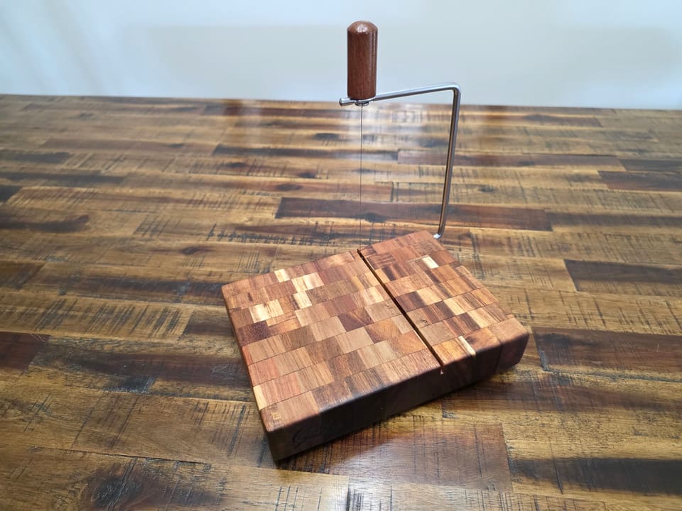Cheese slicer board with the wire raised, standing on a plank table
