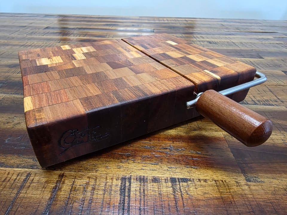 Side view of a dark end-grain slicer board with its wood handle and wire