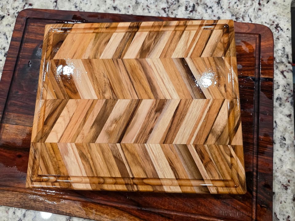 Glossy herringbone serving board with a groove around the edge, reflecting window light