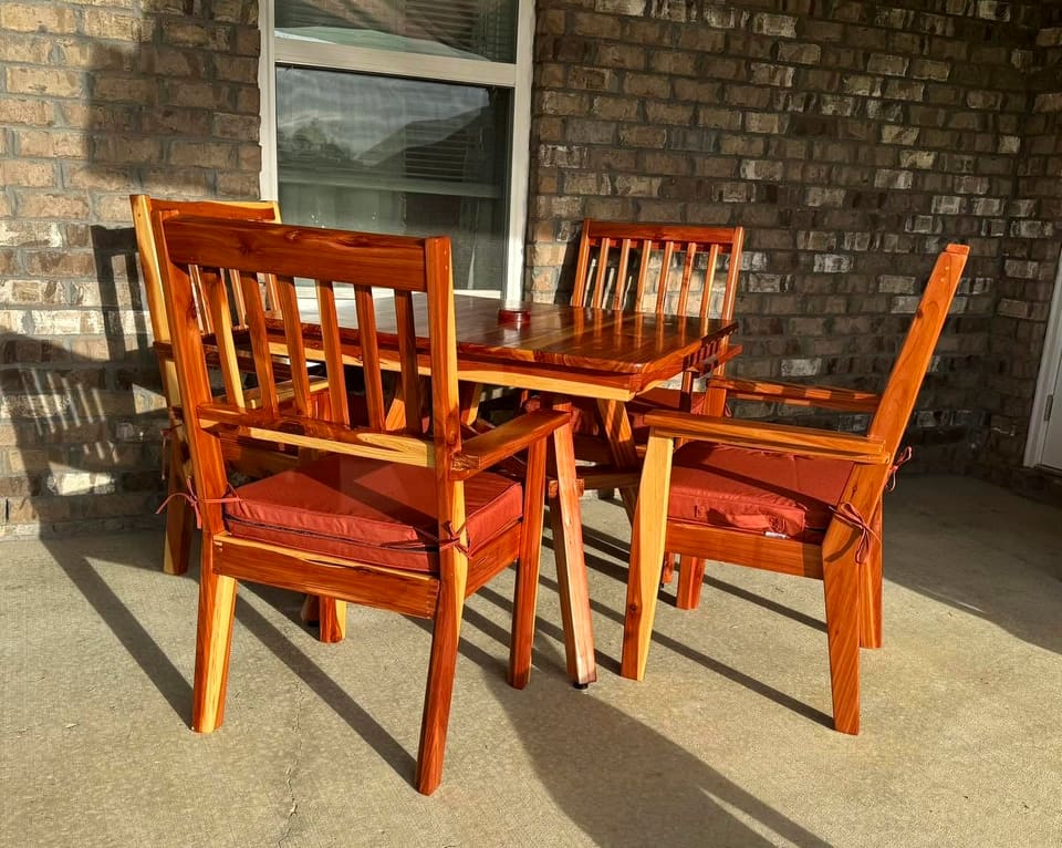 Outdoor dining table and slat-back armchairs with rust-coloured cushions on a covered brick patio