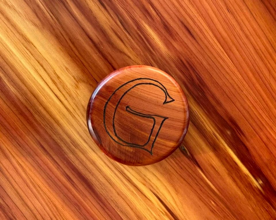 Round wood disc with a letter G burned into the centre